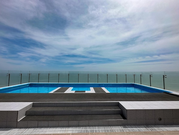 Una piscina con vista al mar, escalones que conducen a ella y un cielo despejado.