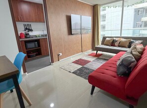 Una sala de estar moderna con un sofá rojo, un televisor de pantalla plana y una cocina con armarios de madera y una máquina de café.