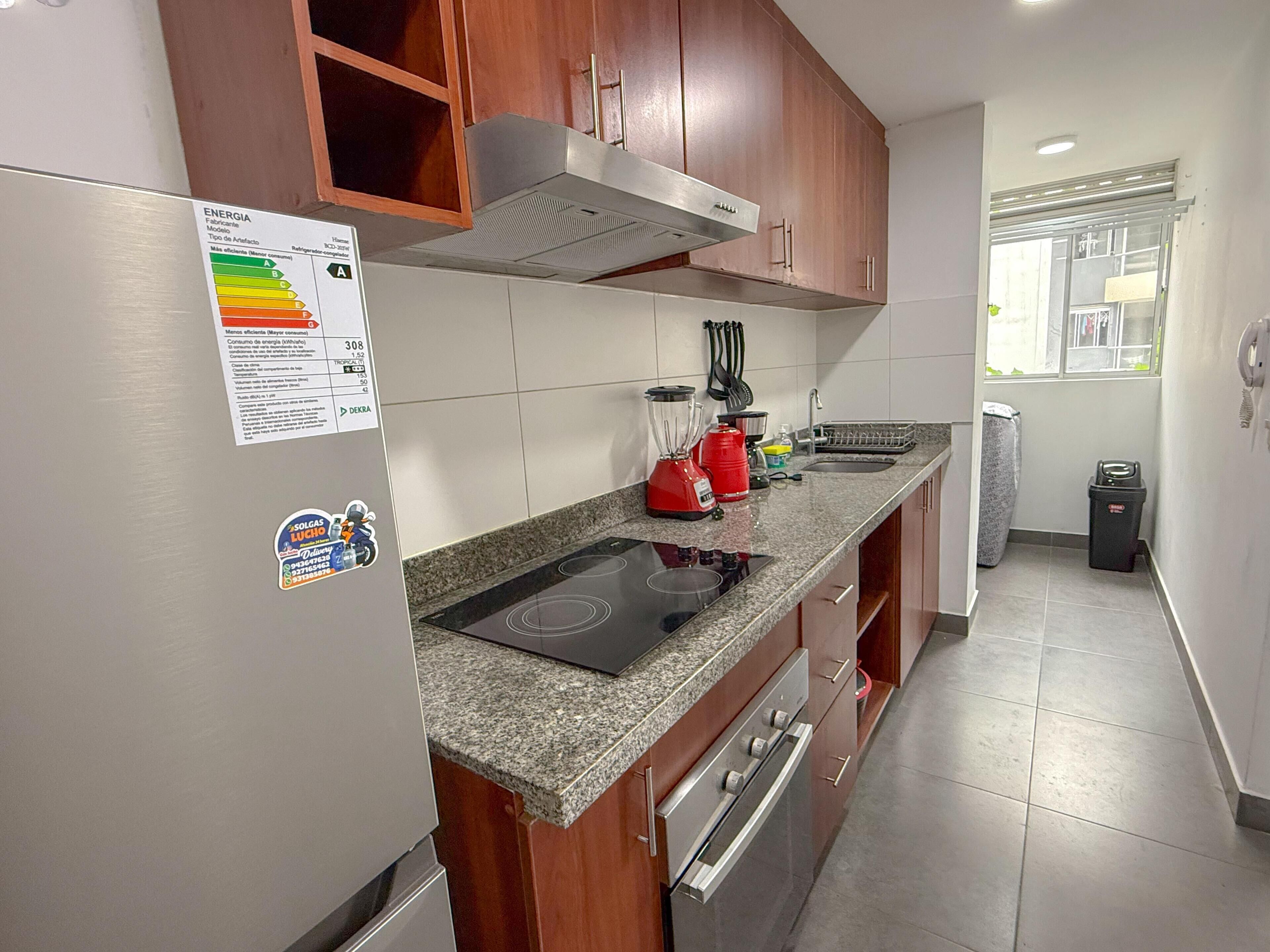 Una cocina con encimera de granito, electrodomésticos de acero inoxidable, armarios de madera y un ventanal que proporciona luz natural.