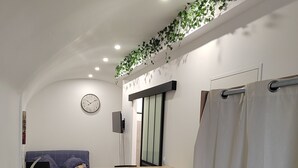 A modern room with a dining table, chairs, a sofa, a clock, and a shower curtain. - Pleasant studio in the heart of town. Close to the A9 and tramway! (Saint-Jean-de-Védas)