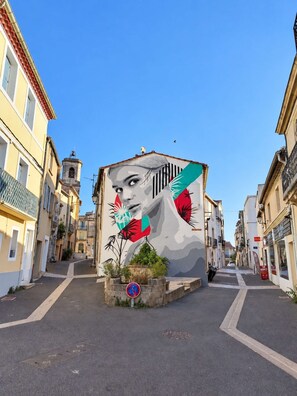 Un carrer amb un mural a un edifici, cel clar i un senyal de prohibició d'estacionament.