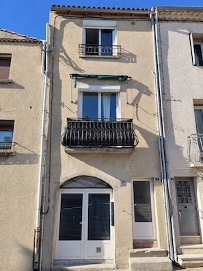 A building with a balcony, a large window, and a door. - Renovated studio in the heart of the village, 7 minutes by tram from Montpellier (Saint-Jean-de-Védas)