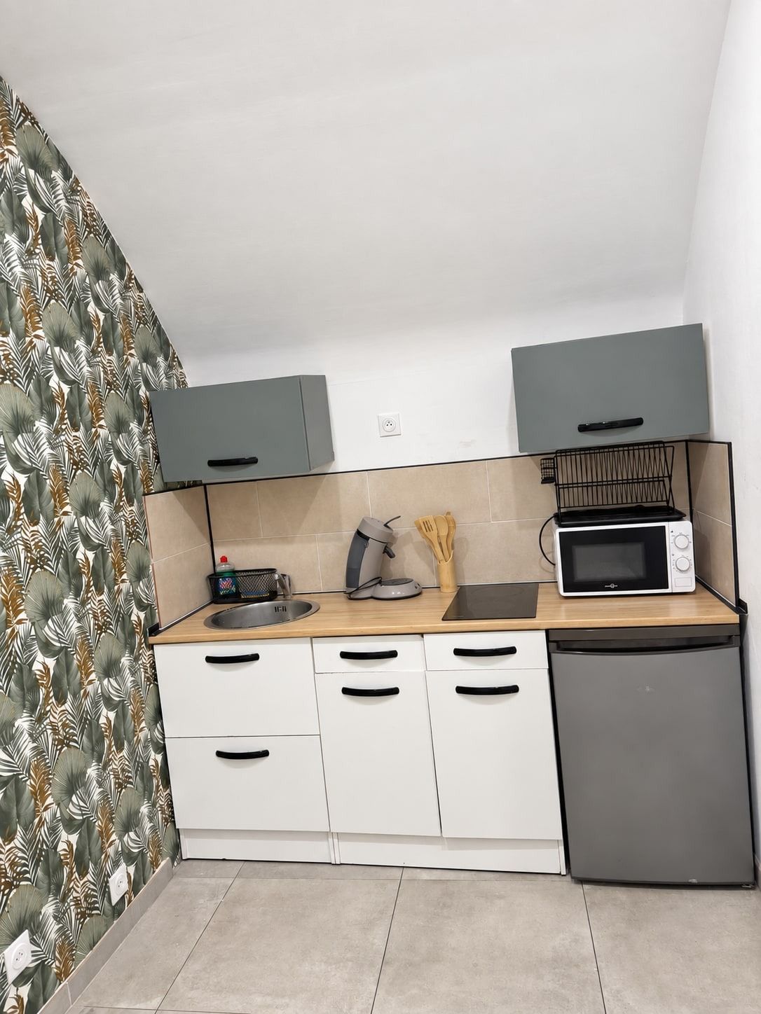 A compact kitchen with white cabinets, a microwave, a toaster, and a small refrigerator.
