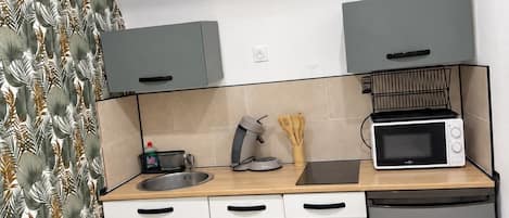 A compact kitchen with white cabinets, a microwave, a toaster, and a small refrigerator.