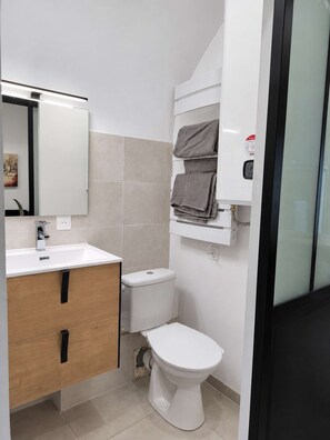 A modern bathroom with a white sink, wooden vanity, a toilet, and a towel rack.