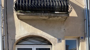 A building with a large arched entrance door, a smaller door to the right, and a balcony with a metal railing above. - Pleasant studio in the heart of town. Close to the A9 and tramway! (Saint-Jean-de-Védas)
