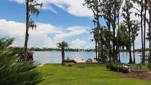 A lakeside property with a grassy lawn, a dock, and tall trees.