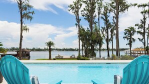 A pool with two turquoise chairs facing the water, surrounded by tall trees and a view of a lake.