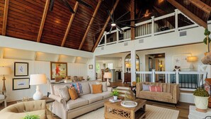 A spacious living area with high ceilings and wooden beams, furnished with sofas, armchairs, and a coffee table.