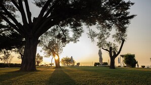 Un parc amb arbres grans i una estàtua al fons.