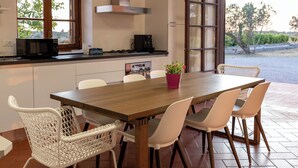 A modern kitchen with a wooden table, white chairs, a potted plant, and a view through an open door. - At 6 km from the sea villa with large pool and large green spaces Ideal for families (sanarica)