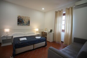 Une chambre d’hôtel avec un lit, un bureau avec un ordinateur portable, une chaise et un canapé.