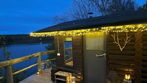 Une cabane en bois dotée d’une terrasse donnant sur un plan d’eau, de guirlandes lumineuses et de lanternes.