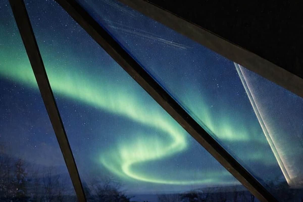 Una habitación con cama, paredes de madera y vistas a las auroras boreales.
