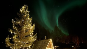 Une cabane au toit en pente, entourée de neige et illuminée par des guirlandes lumineuses.
