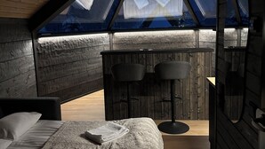 Une chambre avec un plafond en pente, des murs en bois, un lit, deux chaises et une petite table.