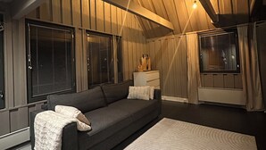 Un salon chaleureux avec un canapé gris foncé, un tapis blanc et des murs recouverts de panneaux en bois.