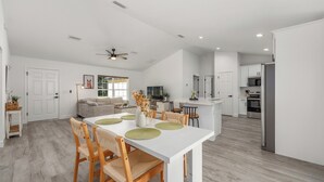 A modern kitchen with white cabinets, a central island, and a dining area with a white table and wooden chairs.
