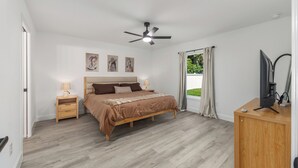 A bedroom with a bed, bedside tables, a ceiling fan, a TV, and a window with curtains.