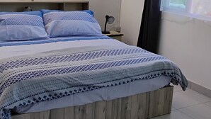 Een slaapkamer met een bed, nachtkastje, wandlamp en raam met gordijn.