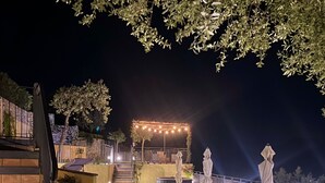 Espaço ao ar livre à noite, com área de estar coberta, degraus de acesso e guarda-corpo.
