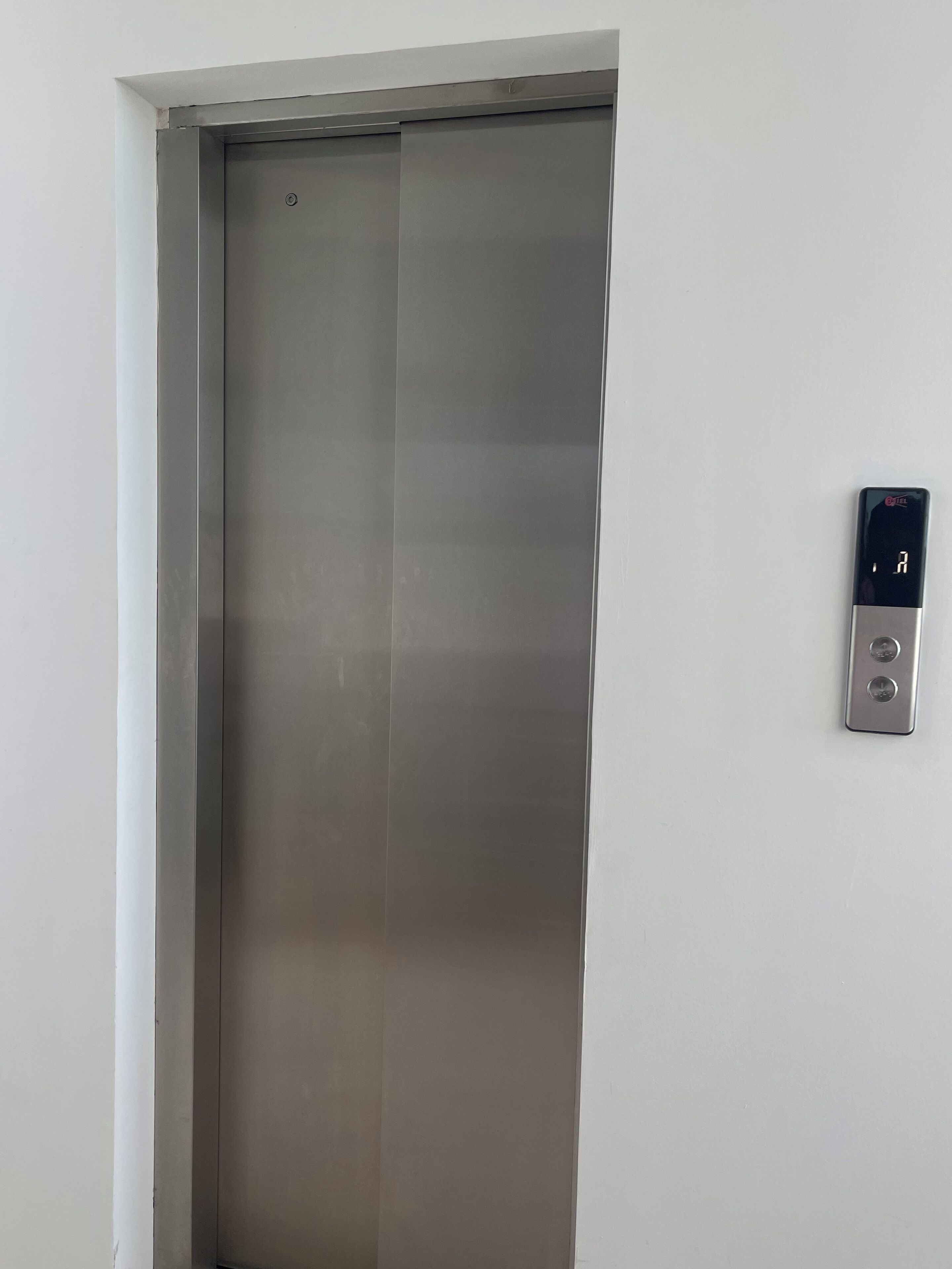 A closed elevator door with a control panel on the wall.