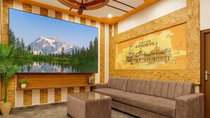 A modern living room with a large flat-screen TV, a sofa, and a coffee table. - Minx Hotels Radhika Palace (Ayodhya)