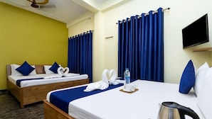 A hotel room with two beds, a flat-screen TV, a kettle, and a water bottle on the beds. - Minx Hotels Radhika Palace (Ayodhya)