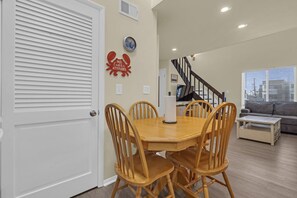 Un coin repas avec une table ronde et quatre chaises, un escalier, un salon avec un canapé et une horloge murale.