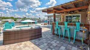 A poolside area with a wicker sofa, teal chairs, and a bar area with a ceiling fan. - Hernando Beach Gulf Access, Dock & Heated Pool (Hernando Beach)