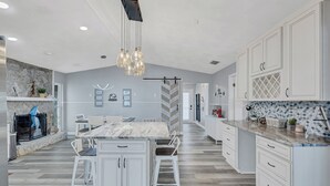A modern kitchen with white cabinetry, a marble countertop, and a central island with bar stools. - Hernando Beach Gulf Access, Dock & Heated Pool (Hernando Beach)