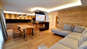 Un salon moderne avec un plancher en bois, un canapé gris, une table à manger avec des chaises et un écran de télévision.