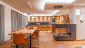Une cuisine moderne avec des meubles en bois, un coin repas doté d’une table en bois et de chaises en cuir, et une cheminée intégrée.