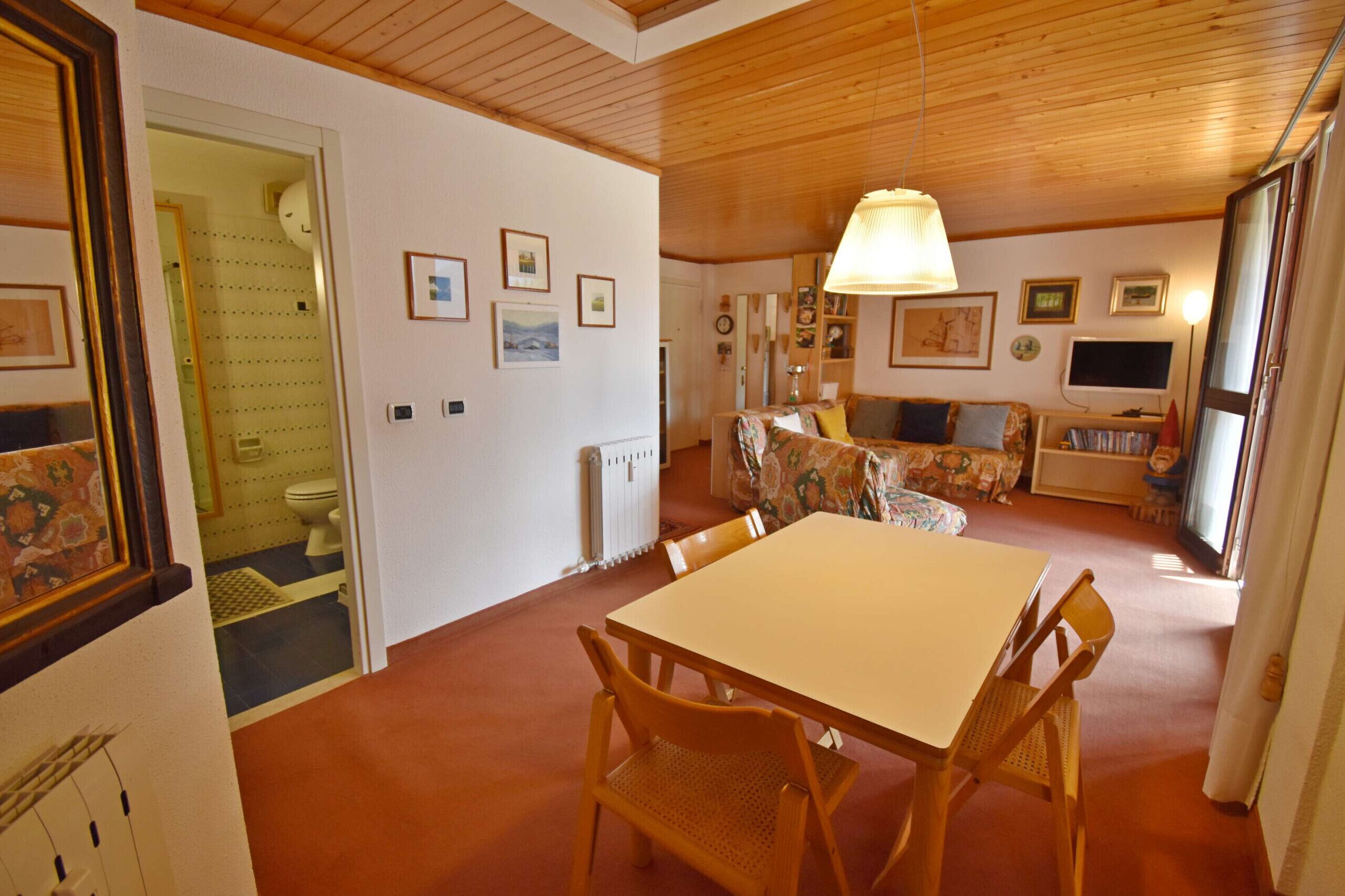 A dining area with a table and chairs, a sofa, a television, and framed pictures on the walls.