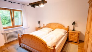 A wooden bed with two nightstands, a radiator, and a window with curtains. - Haus Luise - Cozy vacation apartment with mountain views (Bayrischzell)