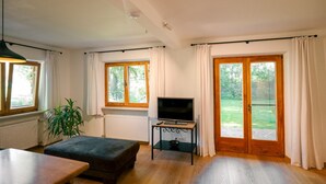A room with a TV on a stand, a plant, and a window with curtains. - Haus Luise - Cozy vacation apartment with mountain views (Bayrischzell)