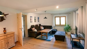 A living room with a sofa, coffee table, and a TV stand. There is a wooden cabinet and a plant. - Haus Luise - Cozy vacation apartment with mountain views (Bayrischzell)