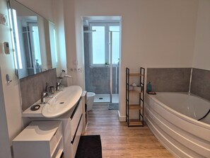 A modern bathroom with a large bathtub, a sink, and a shower area. - A beautiful and very spacious two-bedroom apartment in Bretteville-sur-Odon, in the Venoix neighborhood of Caen. (Bretteville-sur-Odon)