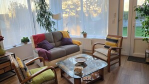 A cozy living room with a sofa, two armchairs, a glass coffee table, and a large window with sheer curtains.