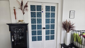 A room with a black cabinet with glass doors, a white door with blue patterned glass panels, and a small black table with a white vase.