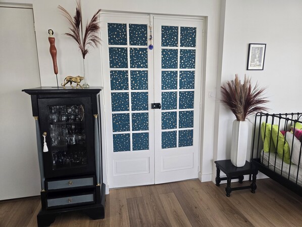 A room with a black cabinet with glass doors, a white door with blue patterned glass panels, and a small black table with a white vase.