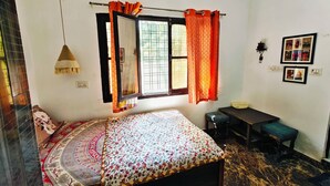 A bedroom with a bed, a desk, a chair, a hanging lamp, and a window with curtains. - Home of Lavenia (Rishikesh)
