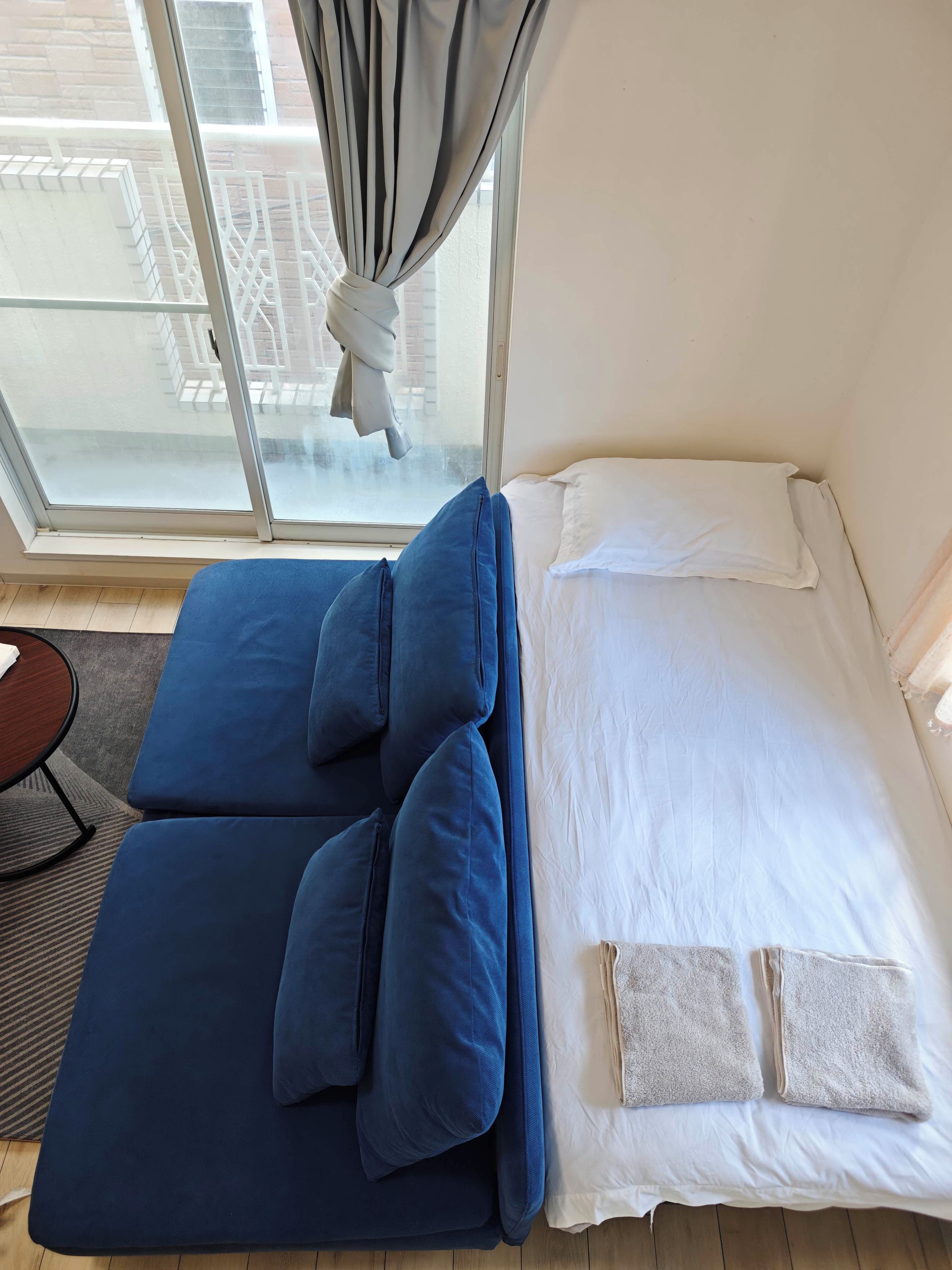 Une pièce avec un lit, un canapé bleu, une petite table et une vue par la fenêtre.