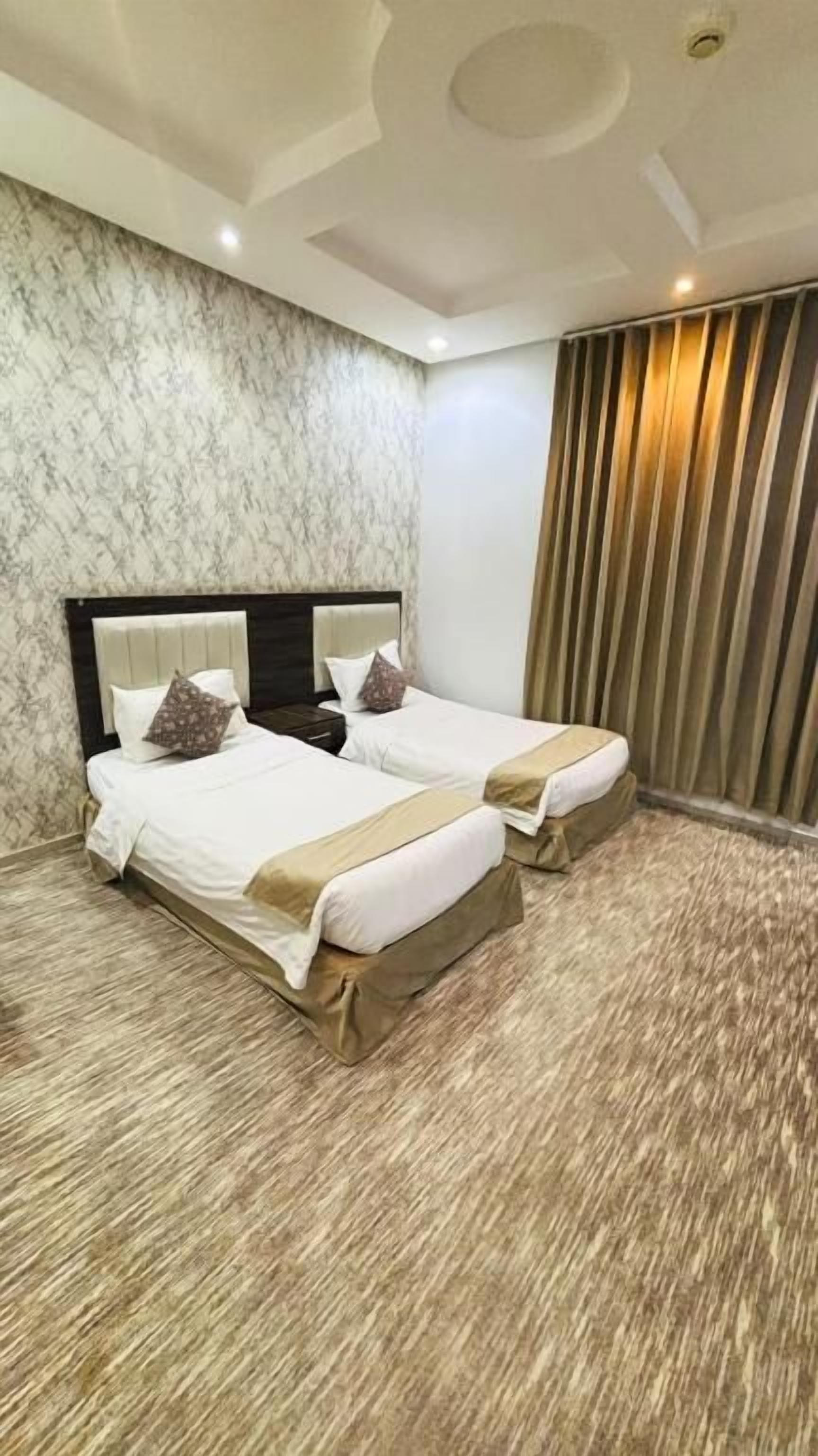 Habitación de hotel con dos camas, pared con diseño de mármol, alfombra texturizada y cortina en la ventana.