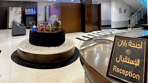 A modern reception area with a marble reception desk, a round seating area, and a staircase in the background. - Razan Home 1 for serviced apartments (Riyadh)