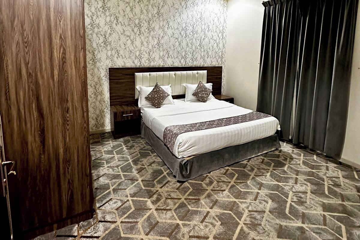 Habitación de hotel con cama, armario, alfombra estampada e iluminación empotrada en el techo.