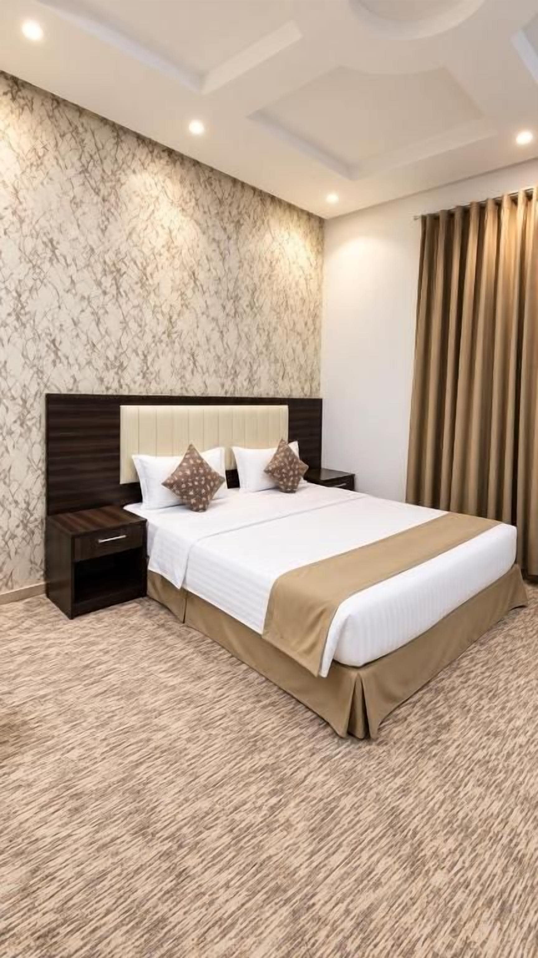Una habitación de hotel con una cama grande, una mesita de noche y un cabecero con un diseño tipo mármol.
