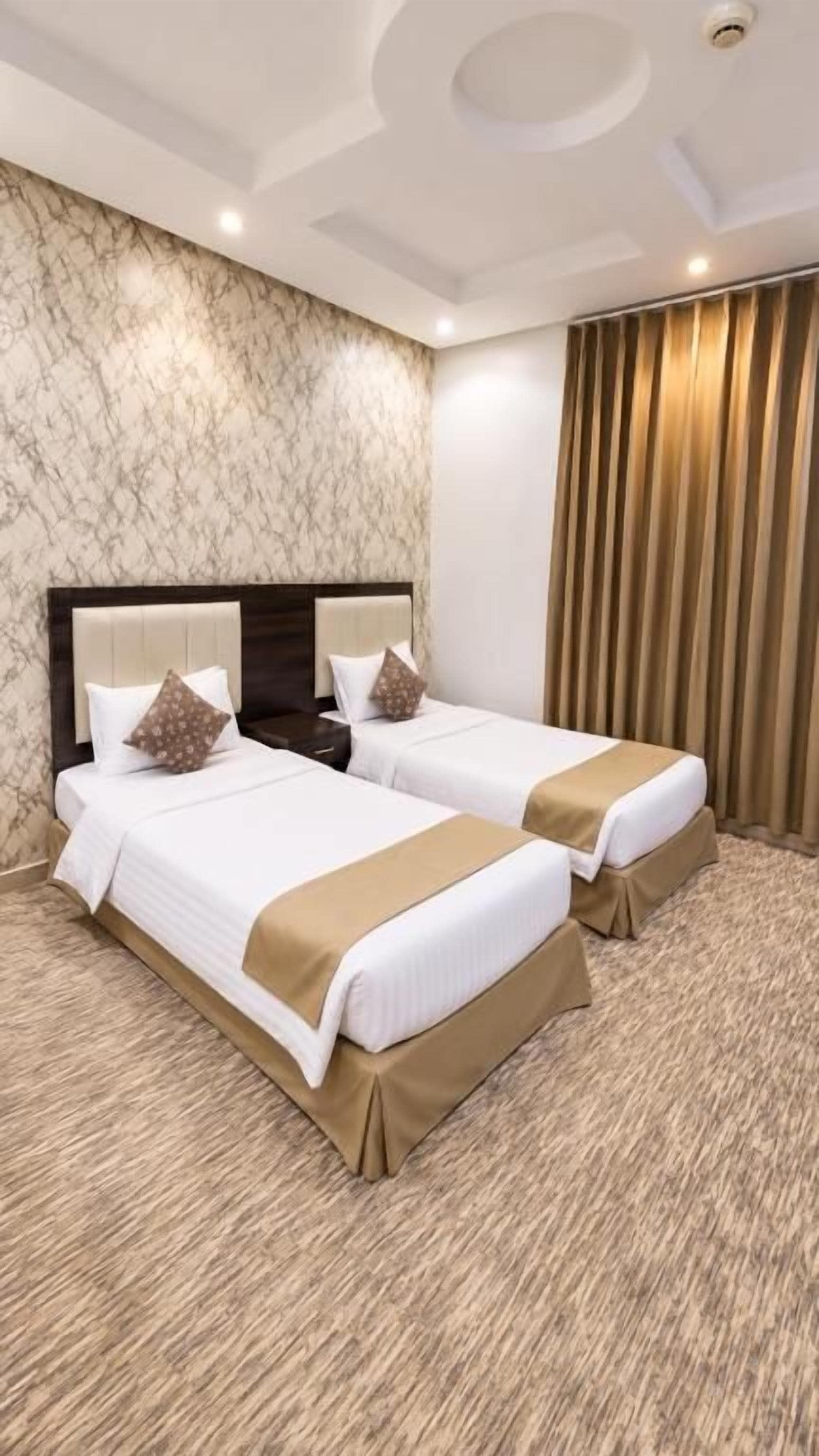 Habitación de hotel con dos camas, una pared de mármol, cabecero de madera y una cortina.