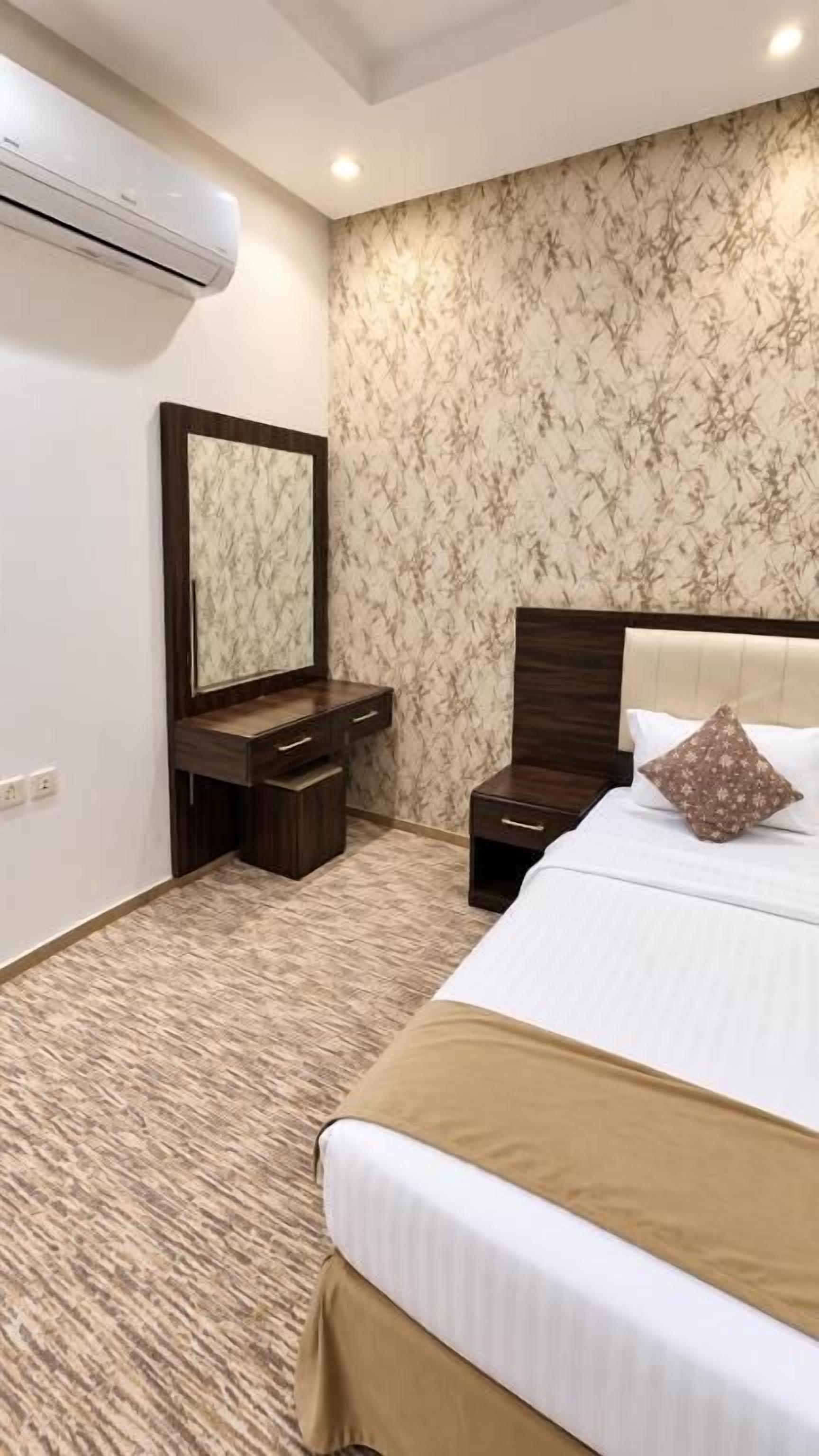 A hotel room with a bed, a nightstand, a dresser, a mirror, and an air conditioning unit.