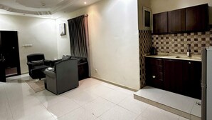A spacious living area with a sofa and a television, a kitchen with dark cabinets and a tiled backsplash, and a ceiling with recessed lighting. - Razan Home 1 for serviced apartments (Riyadh)